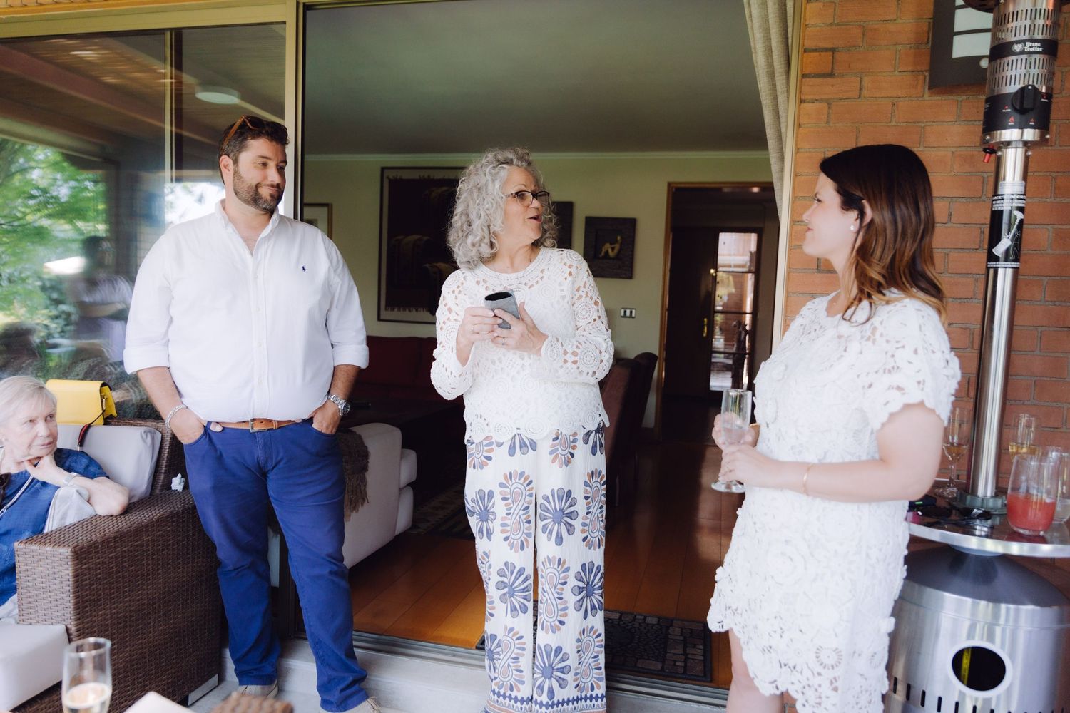 Three people conversing indoors at a casual social event with drinks in hand.