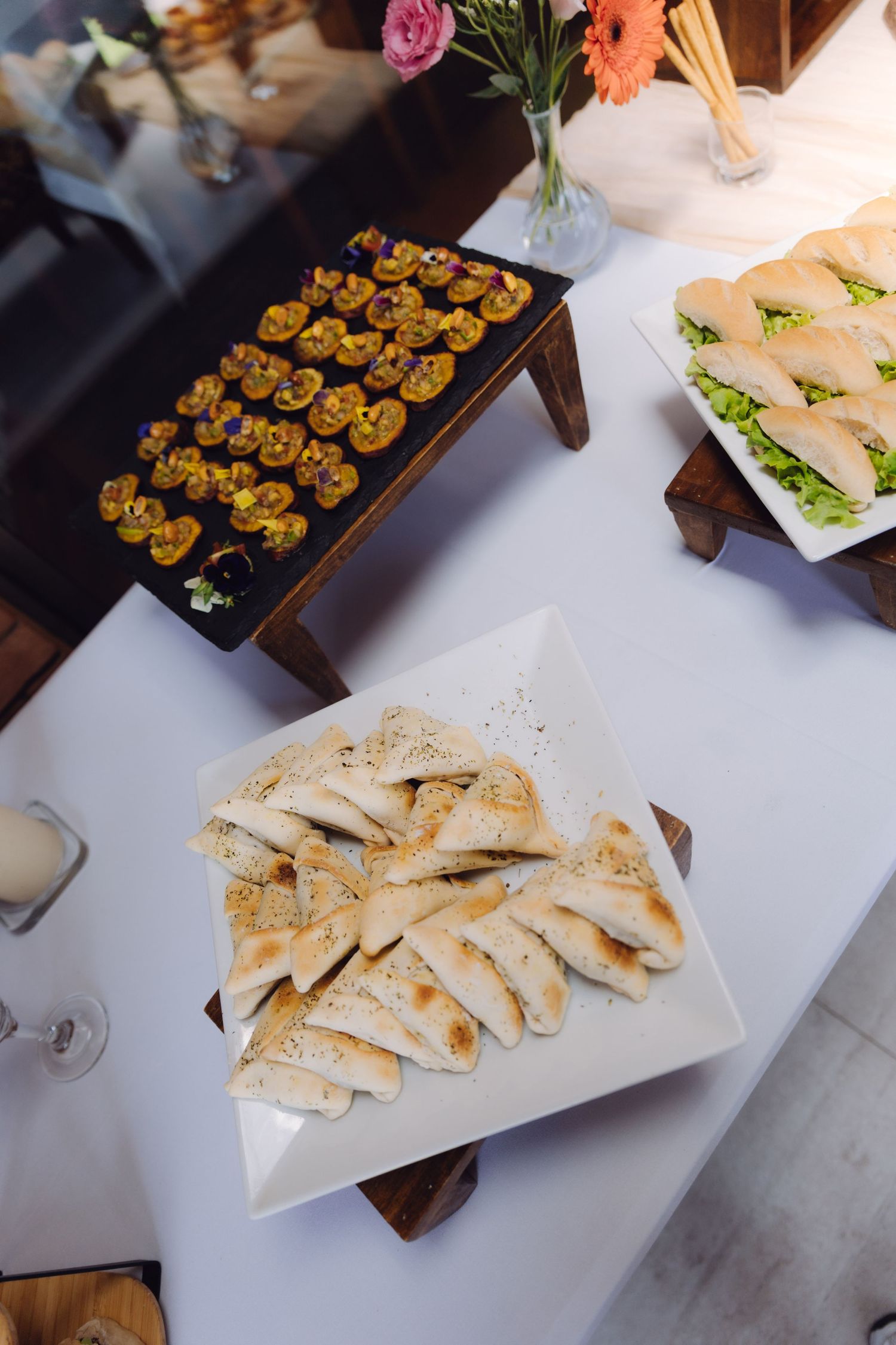 Overhead view of catered appetizers including pita bread, mini sandwiches, and canapes on white platters.