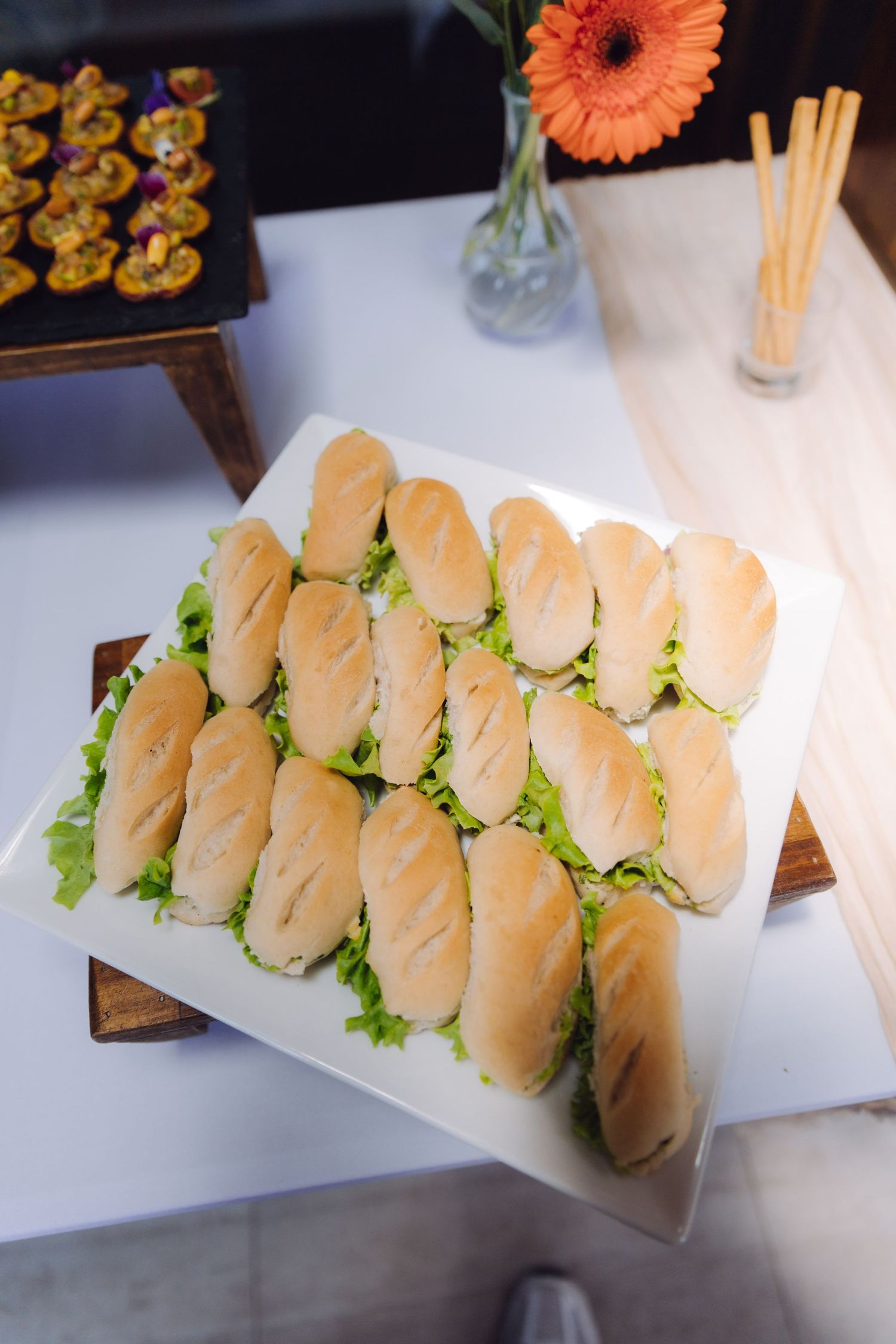 Neatly arranged mini sub sandwiches with lettuce on a white platter at a catered event.