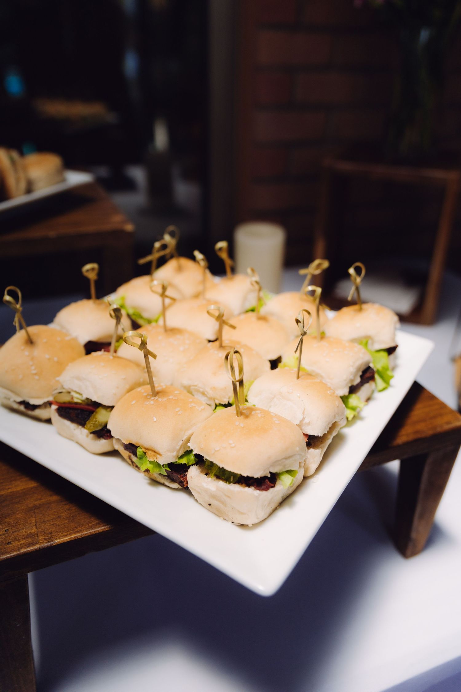 Platter of mini sliders with toothpick garnishes served on a white plate at a catered event.