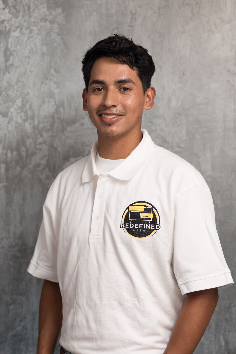 Young man smiling in white Redefined polo shirt against gray concrete background.
