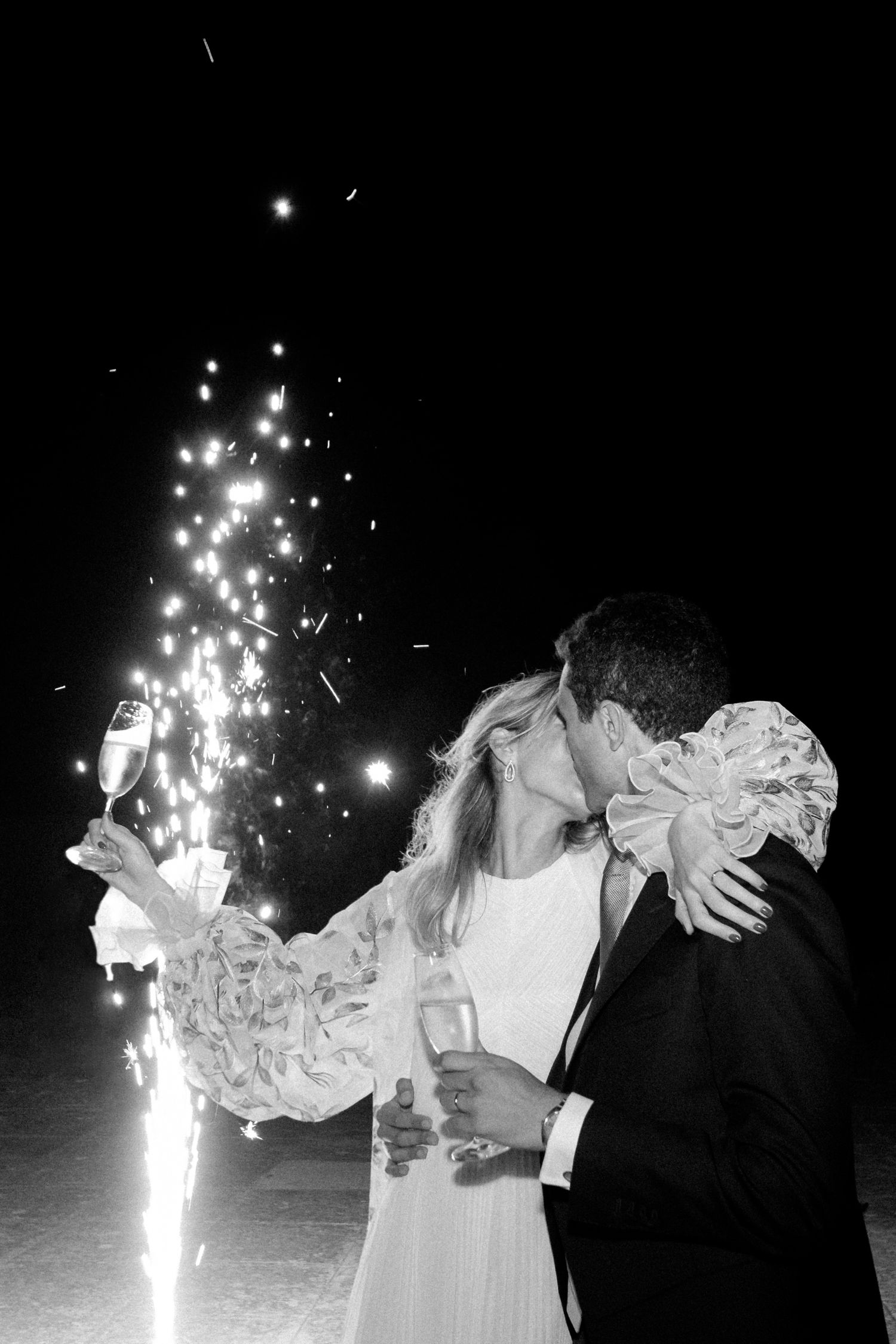 Romantic couple kissing with sparklers in black and white wedding photo.