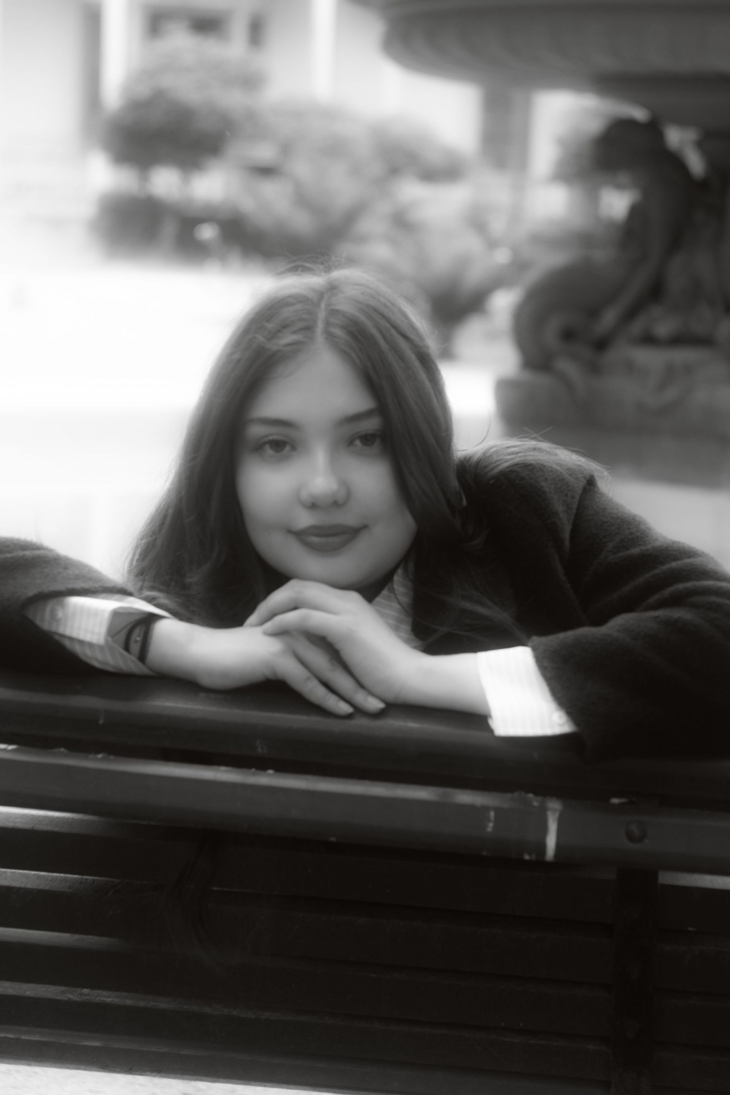 Black and white portrait of a young woman resting on a bench with a serene expression.