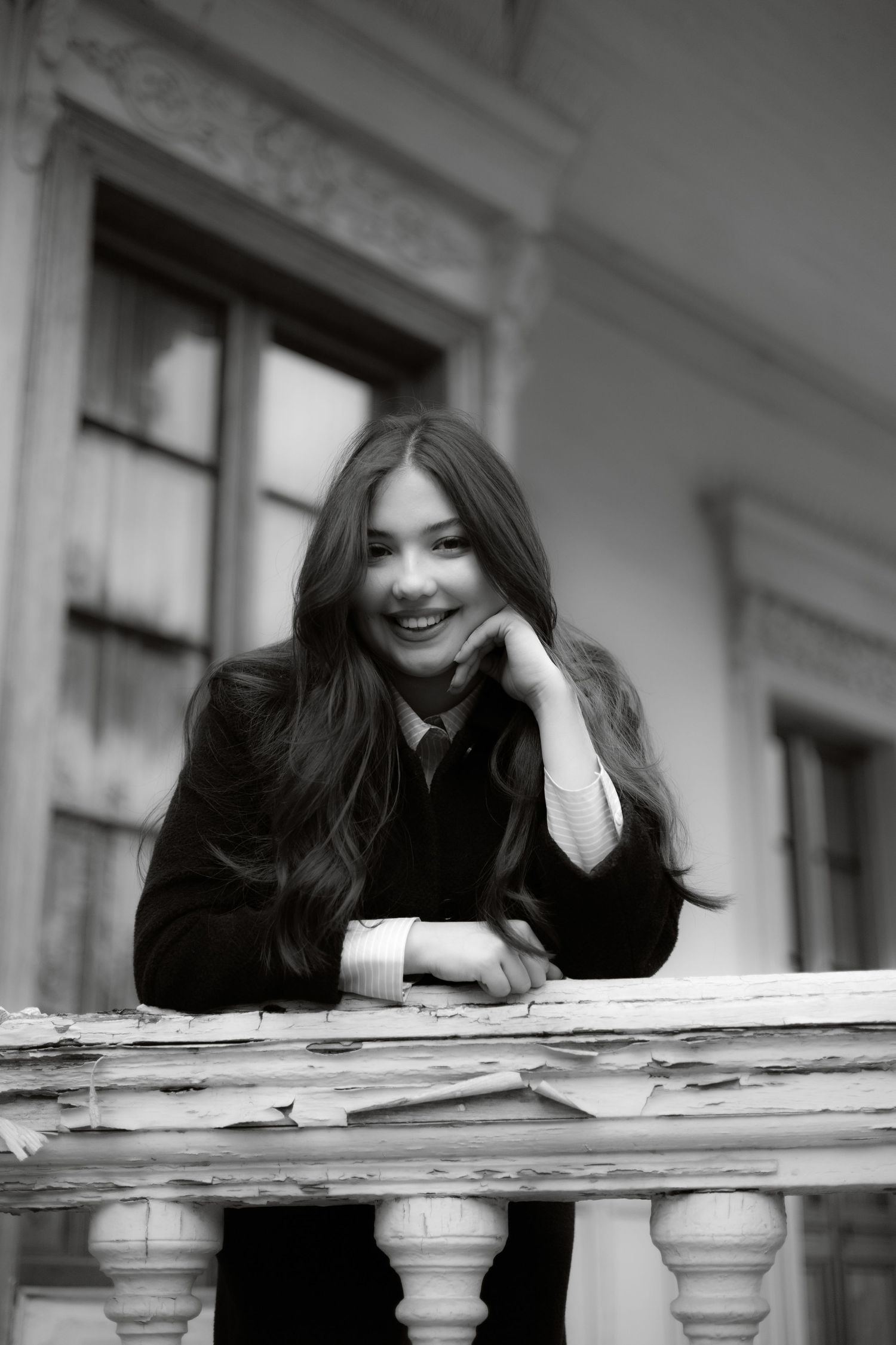 Young woman with long dark hair smiling on a vintage balcony in black and white photo.