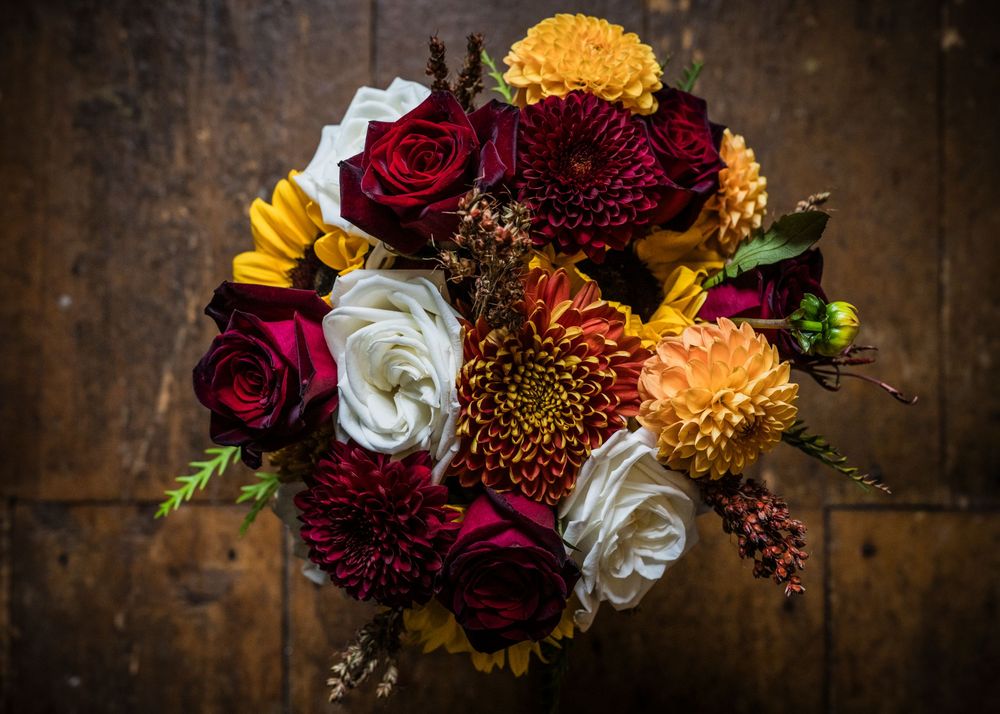 Stunning fall wedding bouquet with burgundy roses, orange dahlias, and white flowers.