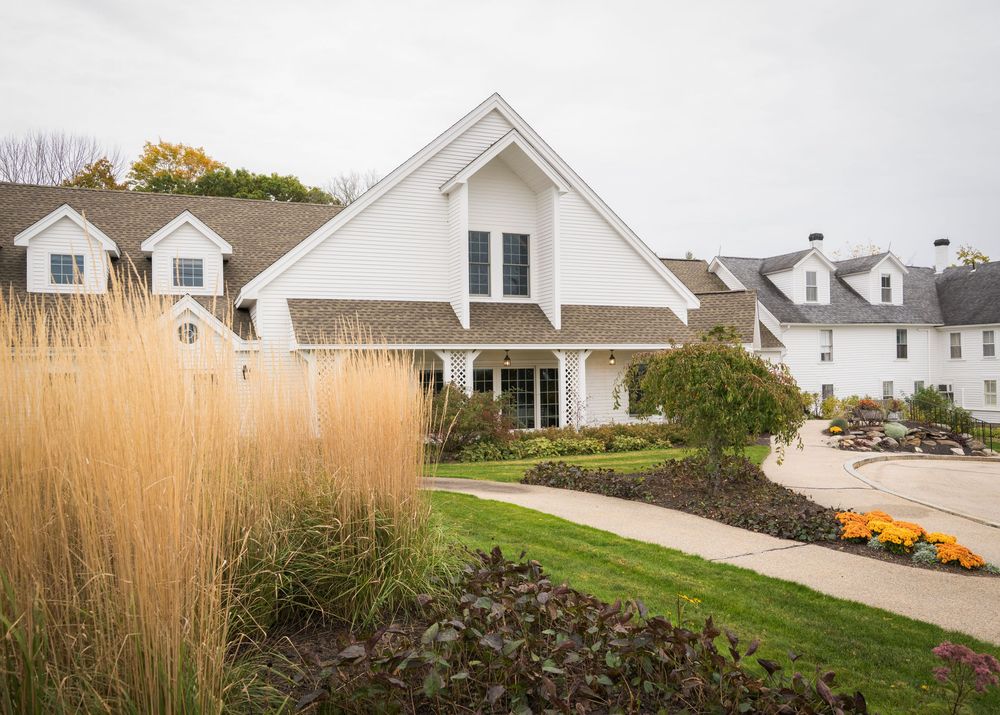 Elegant white farmhouse wedding venue with manicured gardens and ornamental grasses in autumn landscape.