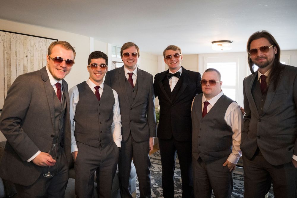 Six men in matching gray suits and sunglasses pose together indoors at a formal event.