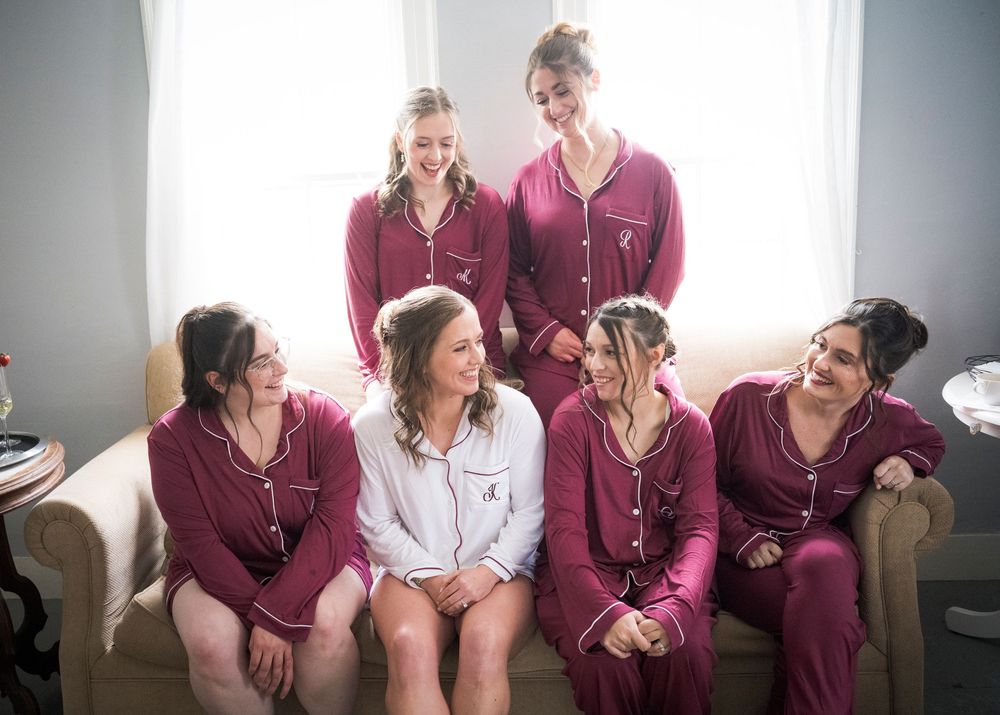 Bride and bridesmaids laughing together in matching burgundy pajamas before the wedding ceremony.
