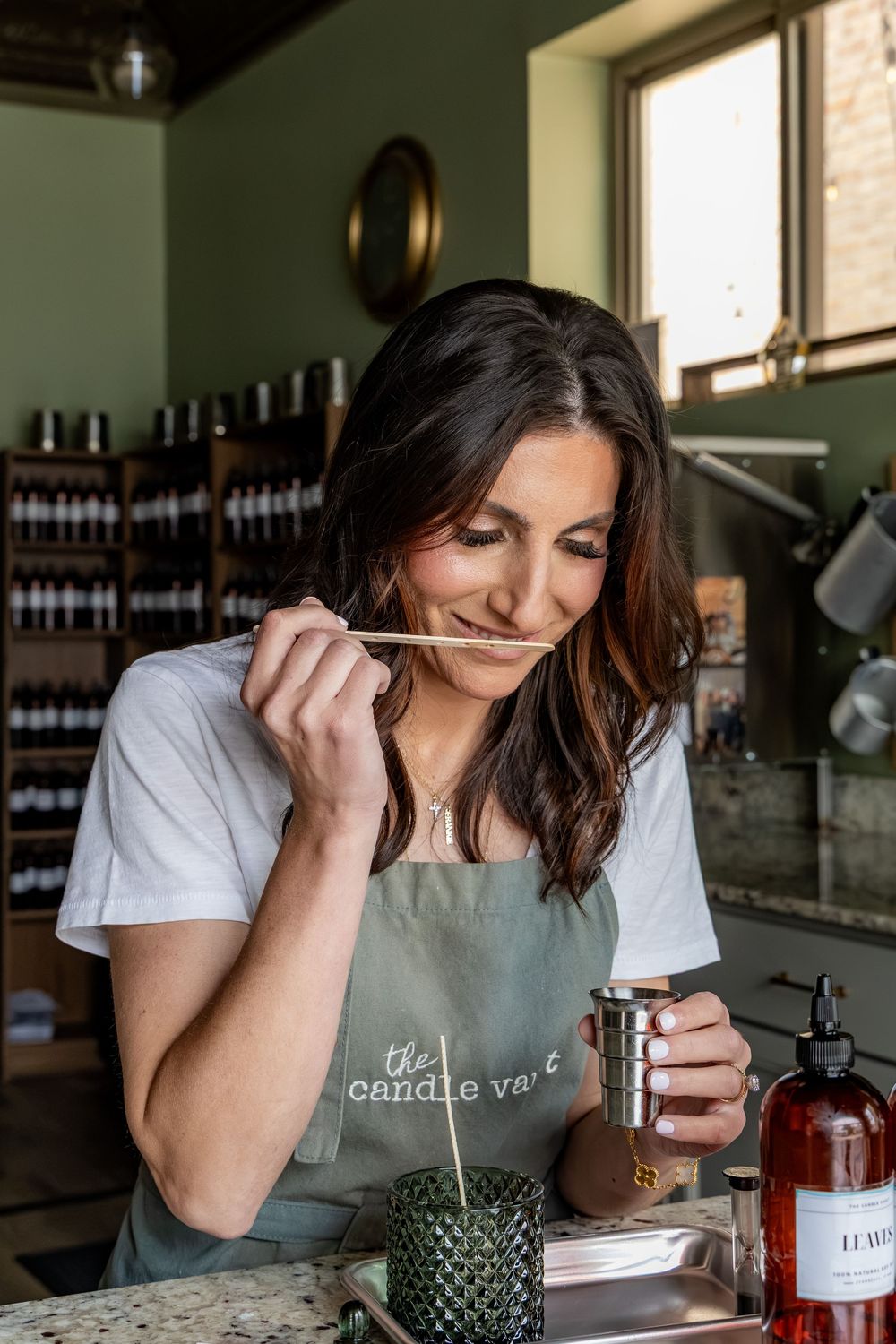 Woman in candle vault apron smelling a wooden wick while crafting candles in a boutique candle shop.