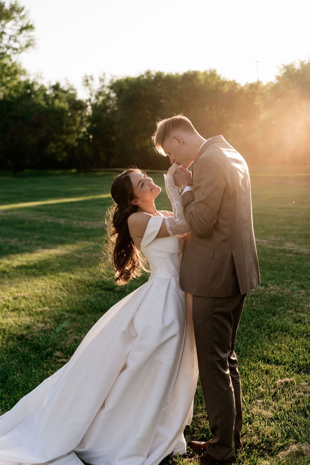 A bride and groom share a romantic moment at golden hour on a lush green lawn, her white gown flowing gracefully.
