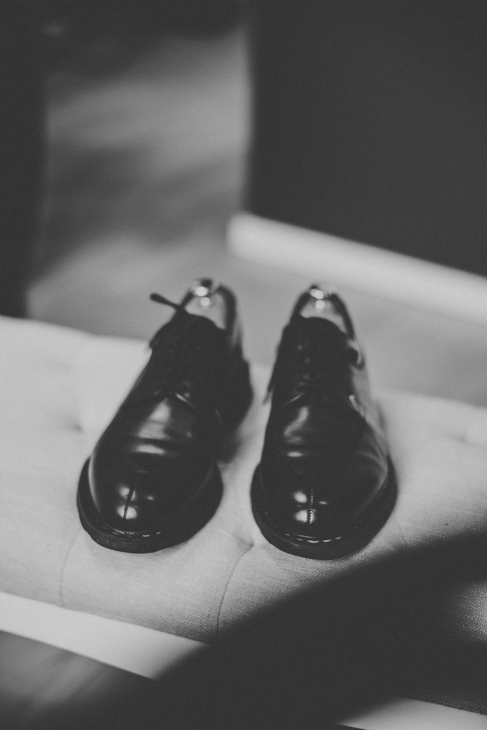 Black and white photo of polished men's oxford dress shoes with laces on a white surface.