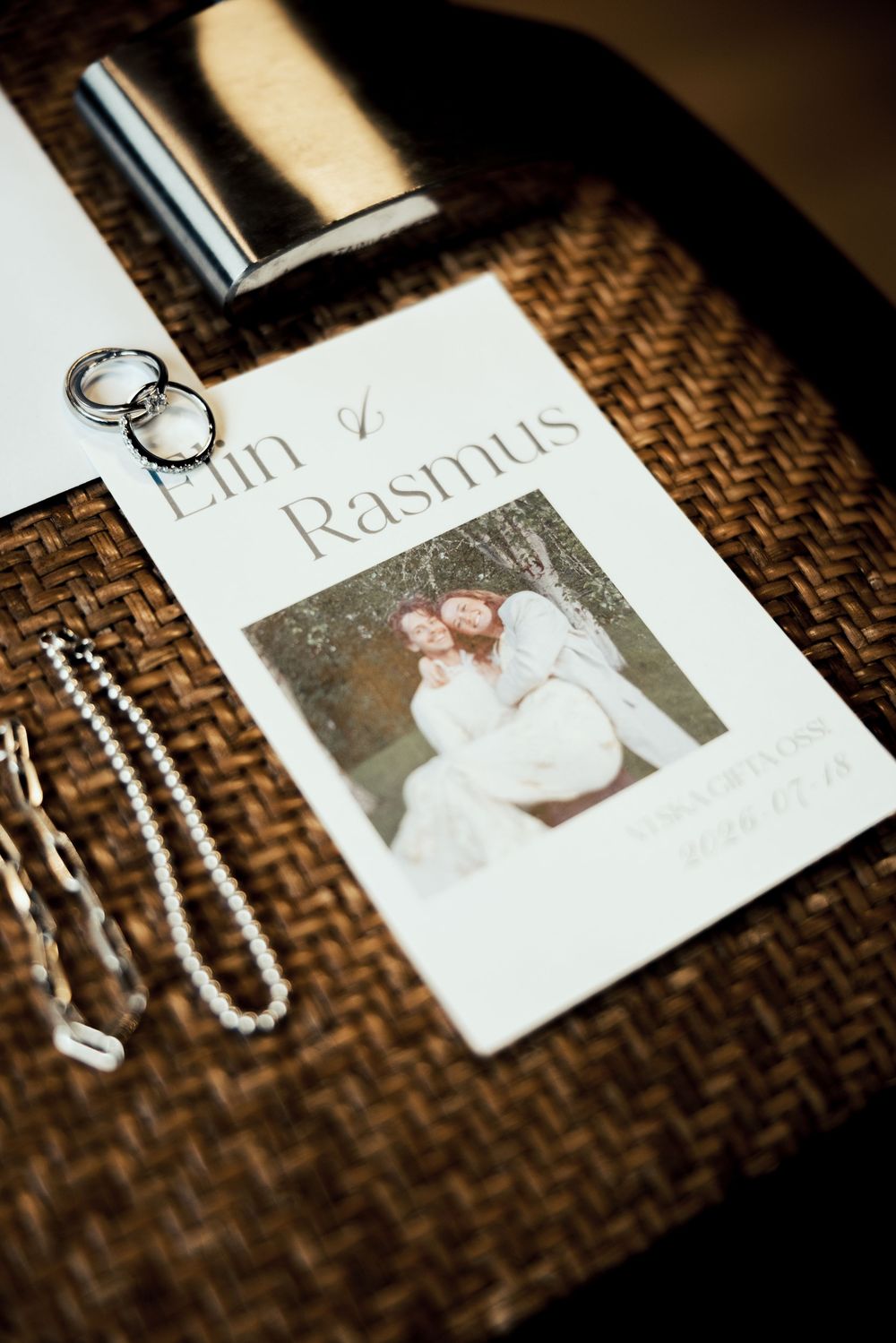 Wedding card for Elin and Rasmus with a couple photo, displayed beside rings, a necklace, and a silver flask.
