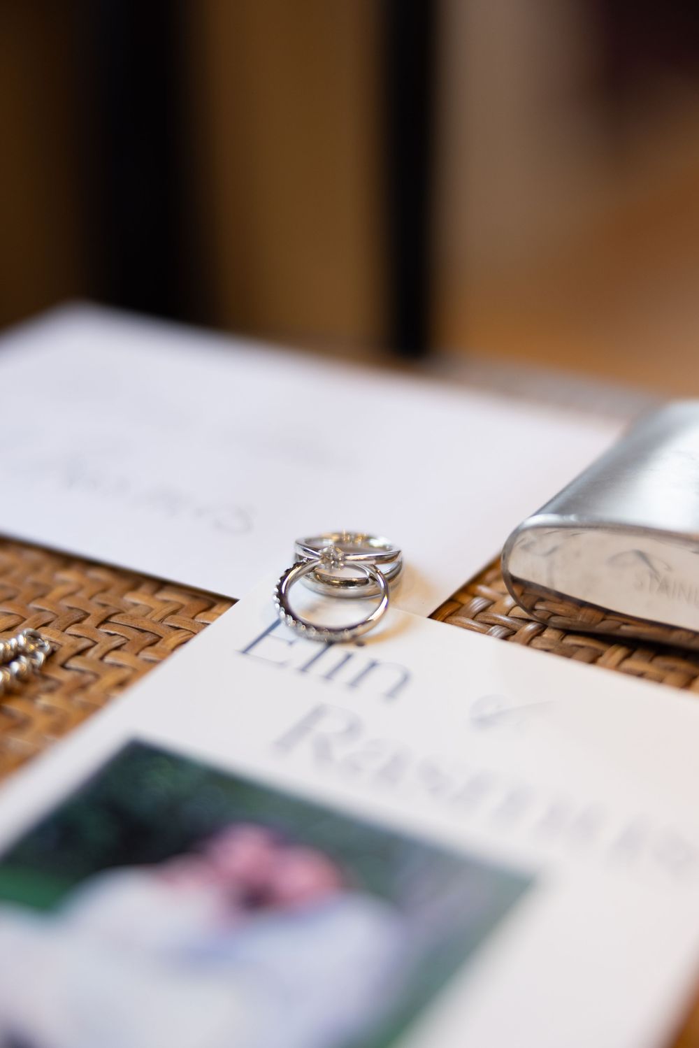 Silver wedding rings stacked on wedding invitation cards for Elin and Rasmus on a woven surface.