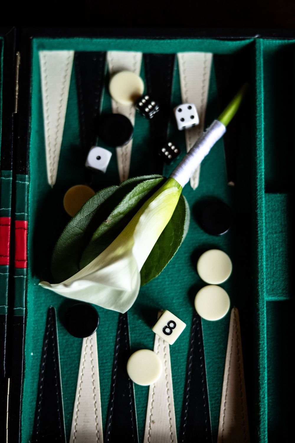White calla lily boutonniere resting on a green backgammon board with black and white checkers and dice.