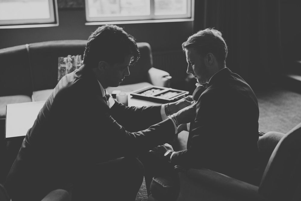 Two men in suits sit together at a table in a dimly lit room, engaged in a serious conversation.