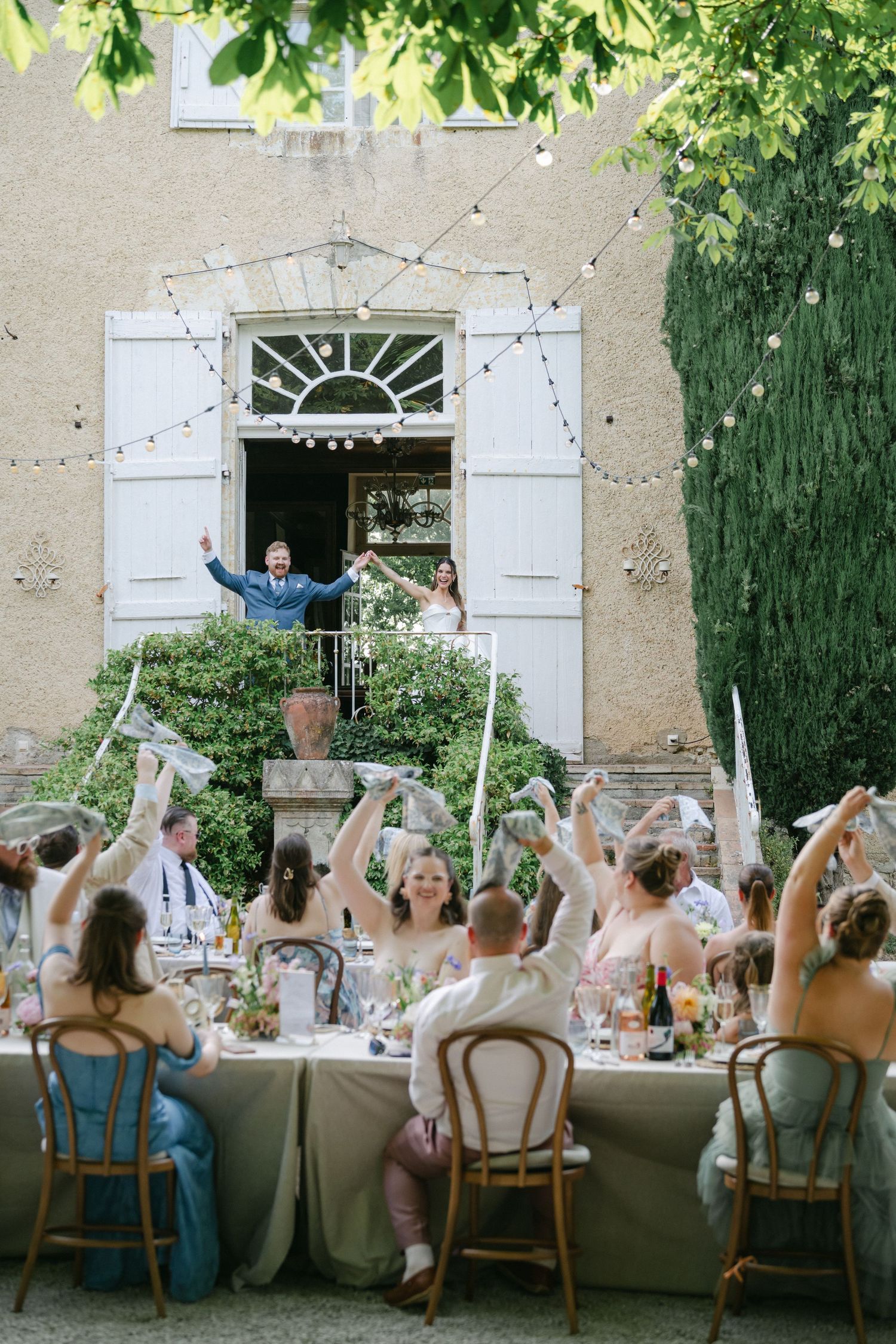 Bride and groom walking through elegant white garden gates surrounded by lush green trees on their wedding day.