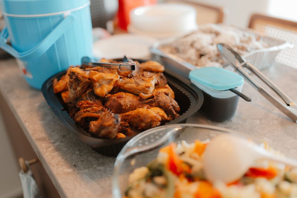 A platter of glazed chicken wings served alongside rice and vegetable salad on a kitchen counter.