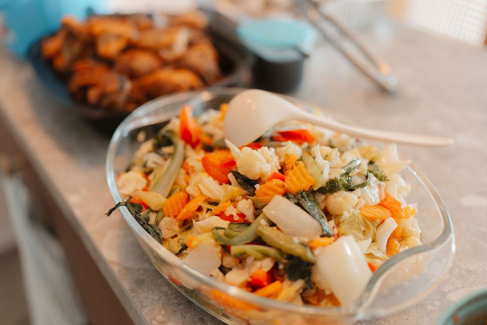 Fresh colorful vegetable salad in a glass bowl with carrots, peppers, and greens served at a buffet.