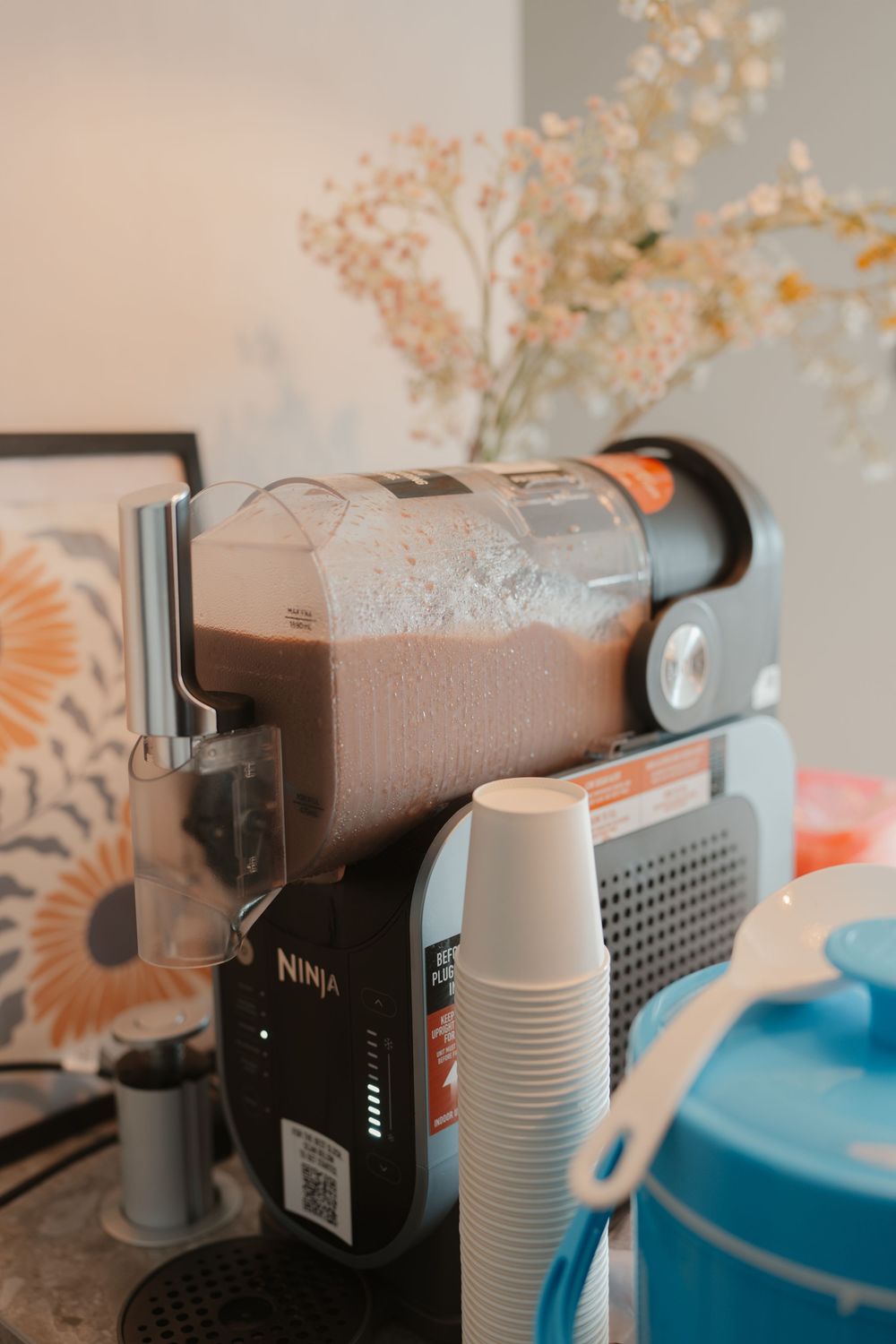 Ninja coffee maker brewing a frothy chocolate drink on a kitchen counter with floral decor.
