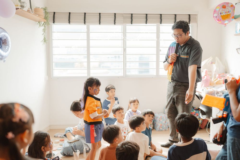 A man entertains a group of young children at an indoor birthday party in a bright, decorated room.
