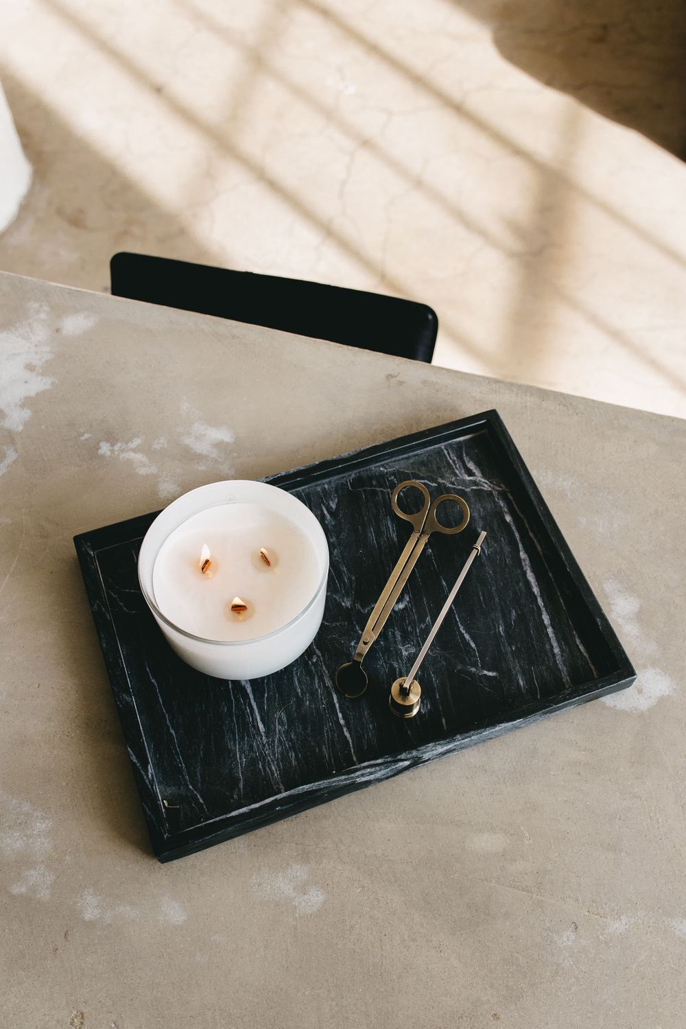 a three wick burning candle on a marble tray with wick cutters