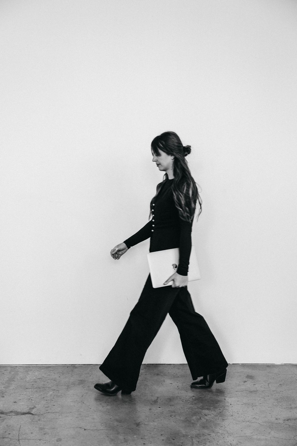 woman with long hair walking quickly, while holding her laptop by her side
