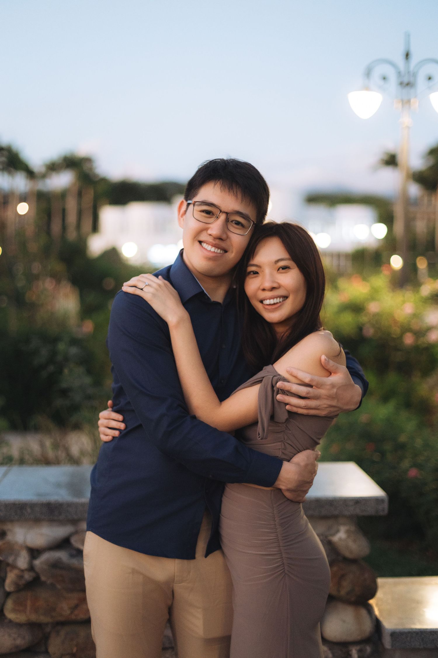 A smiling couple in white outfits sitting on vintage shop steps surrounded by plants and old utility meters.