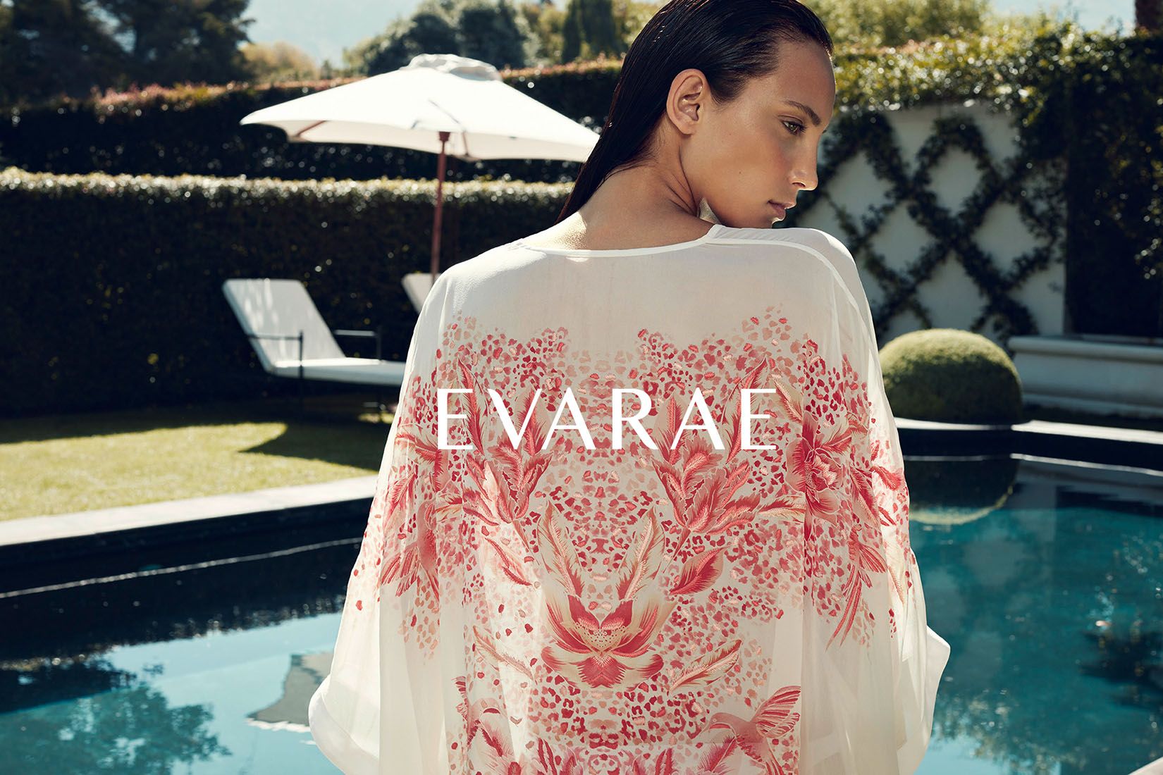 Model wearing white kimono with red floral print standing poolside, EVARAE brand campaign.