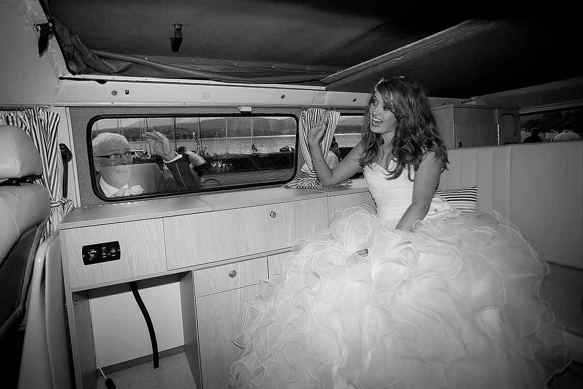 Bride in a white wedding gown sitting inside a vintage VW bus, captured in elegant black and white photography.