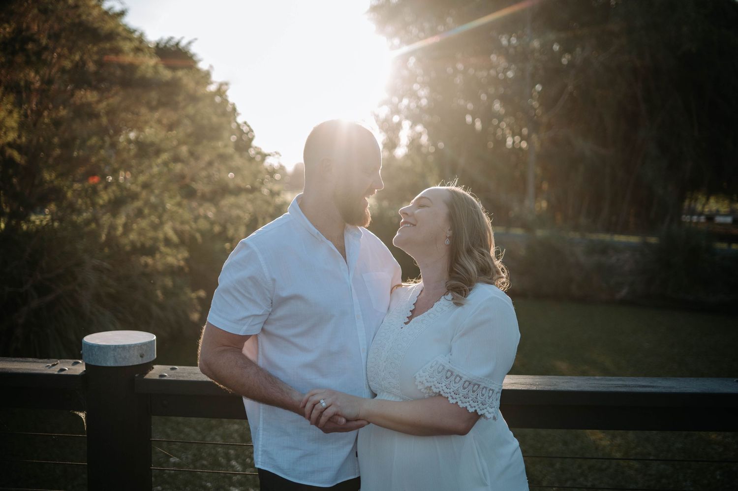 Couple sharing a romantic moment outdoors at golden hour, backlit by warm sunlight with lush greenery behind them.