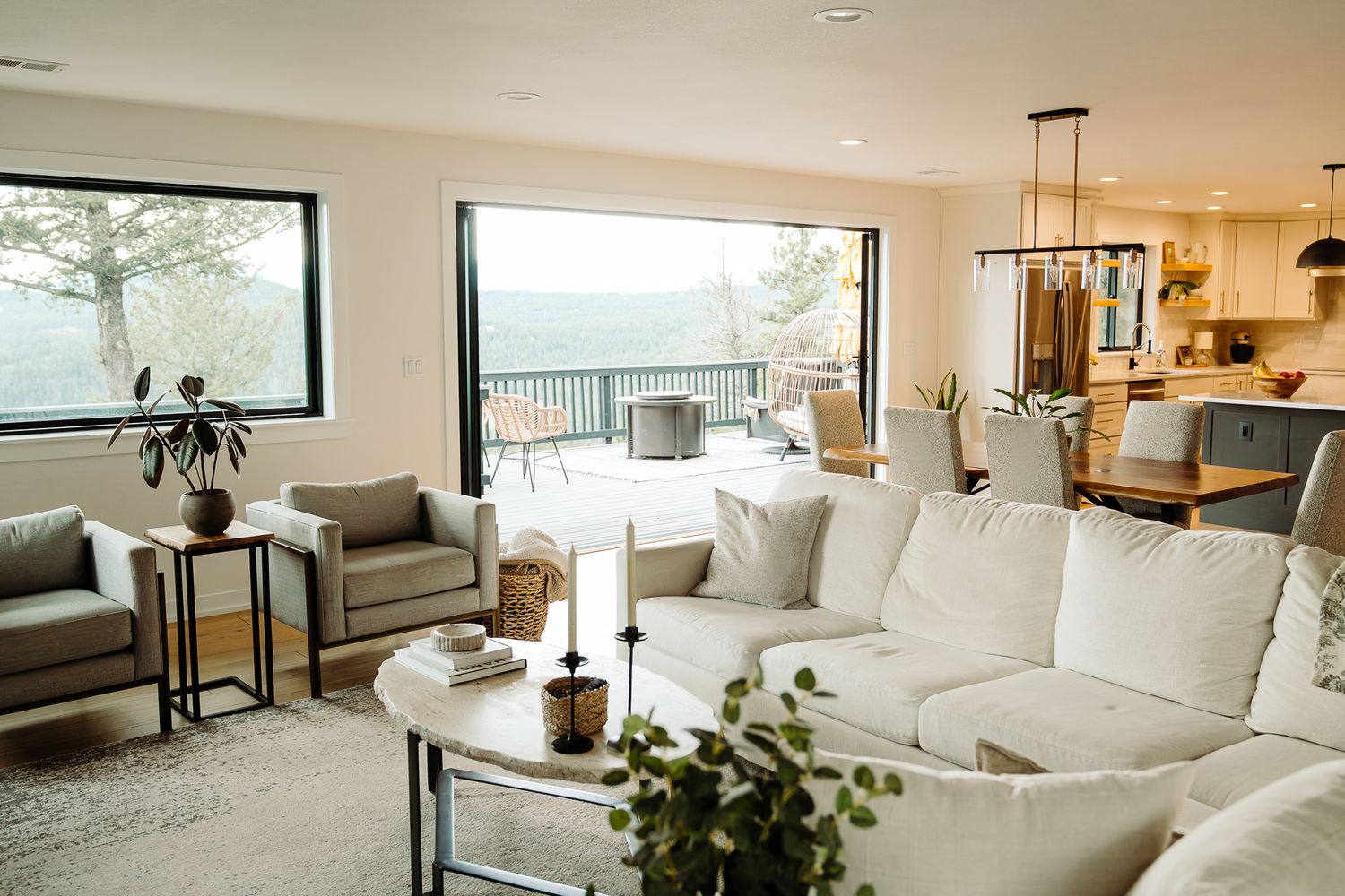 Modern open-plan living room with white sectional sofa, large windows, and scenic outdoor patio view.