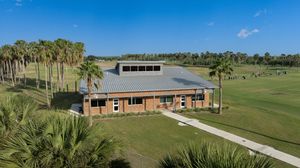 Aerial view of a brick golf clubhouse surrounded by palm trees and lush green fairways.