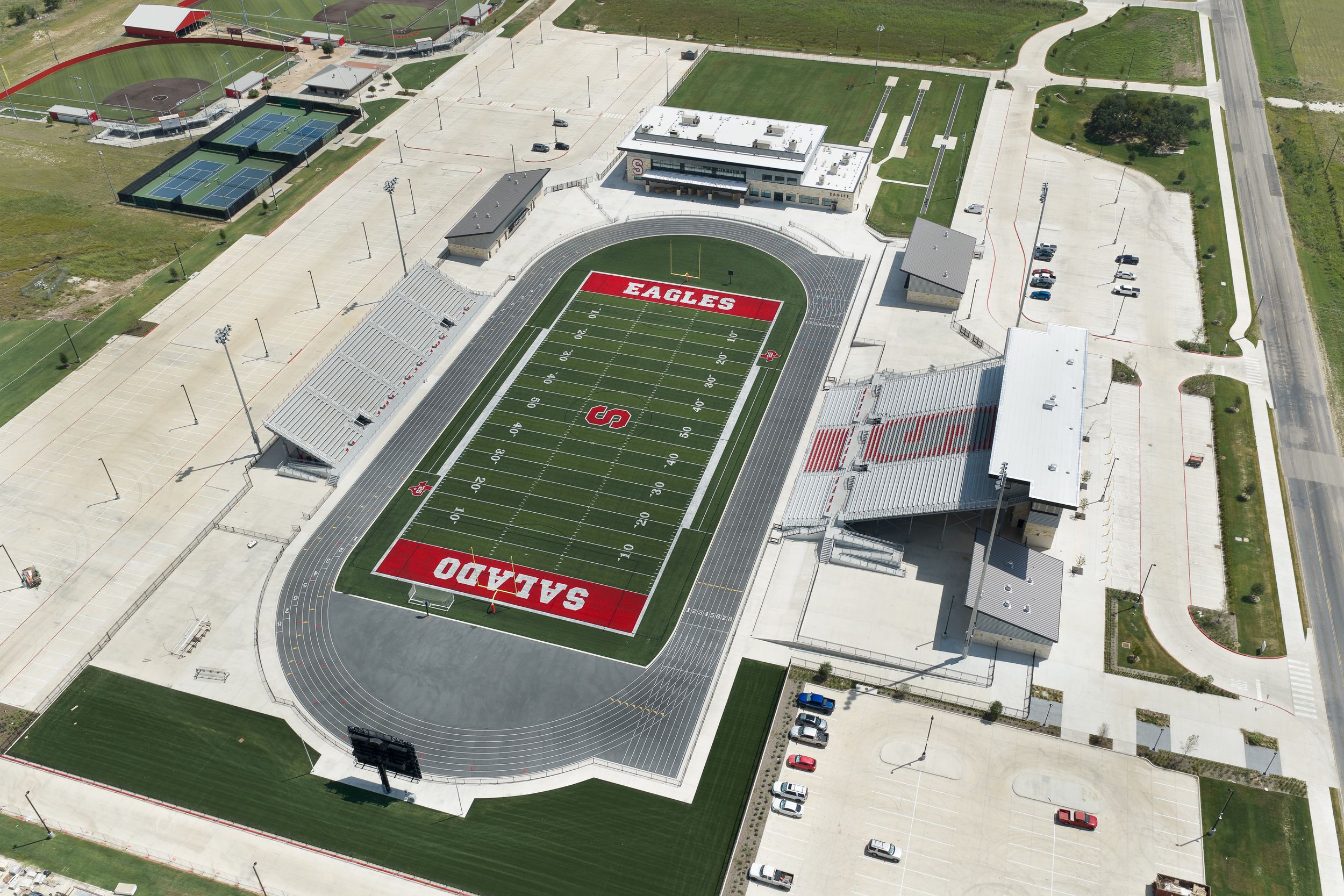 Aerial view of Salado Eagles football stadium with red turf field, track, and school complex at dusk.