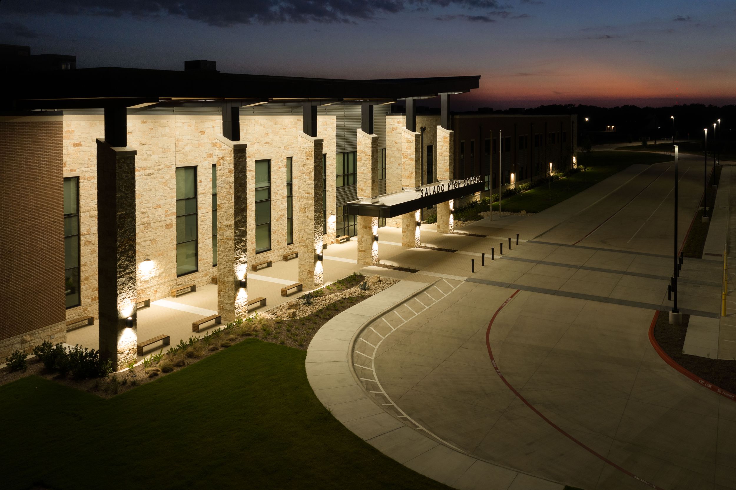 Night view of illuminated Salado ISD school entrance with brick columns and curved walkway.