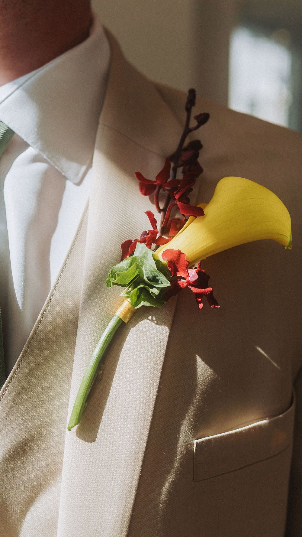 Yellow calla lily boutonniere with red accents pinned to cream wedding suit lapel.