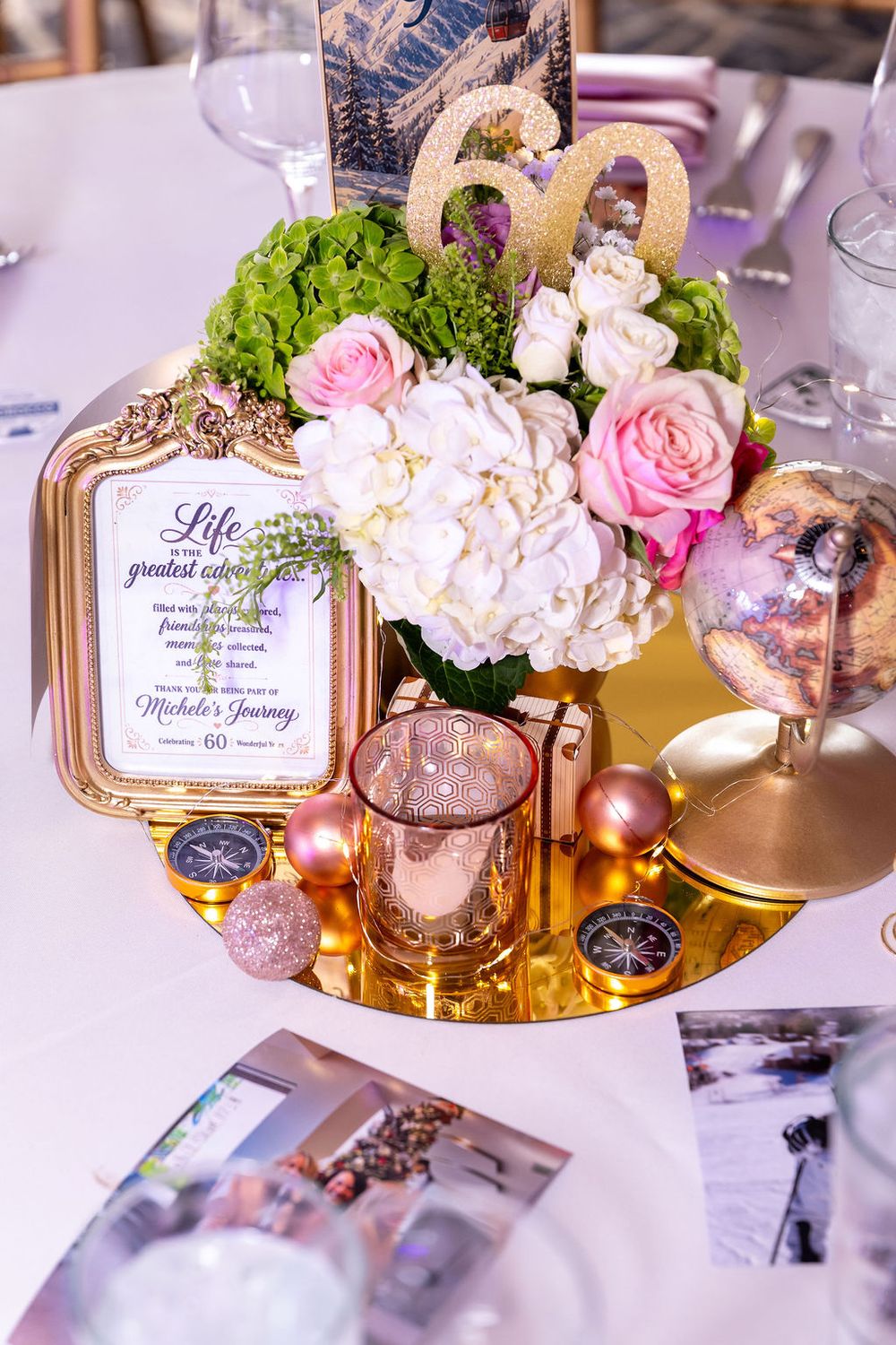 Elegant 60th birthday table centerpiece with pink roses, white hydrangeas, gold mirror, compasses, and framed quote.