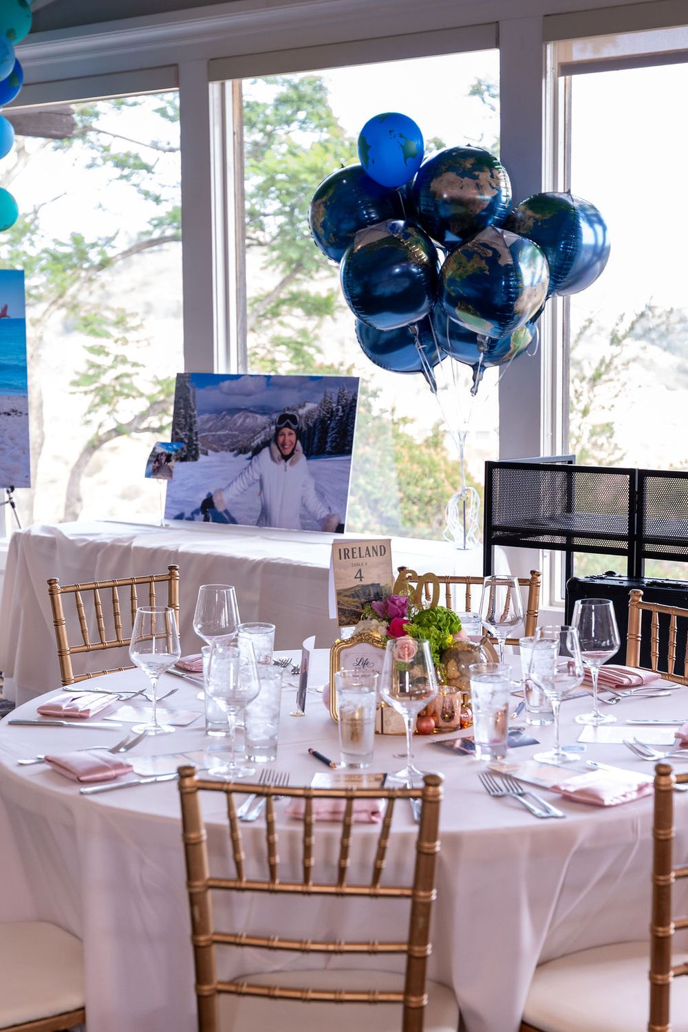 Elegant event table with gold chairs, white linen, globe balloons, wine glasses, and a snowy photo centerpiece.