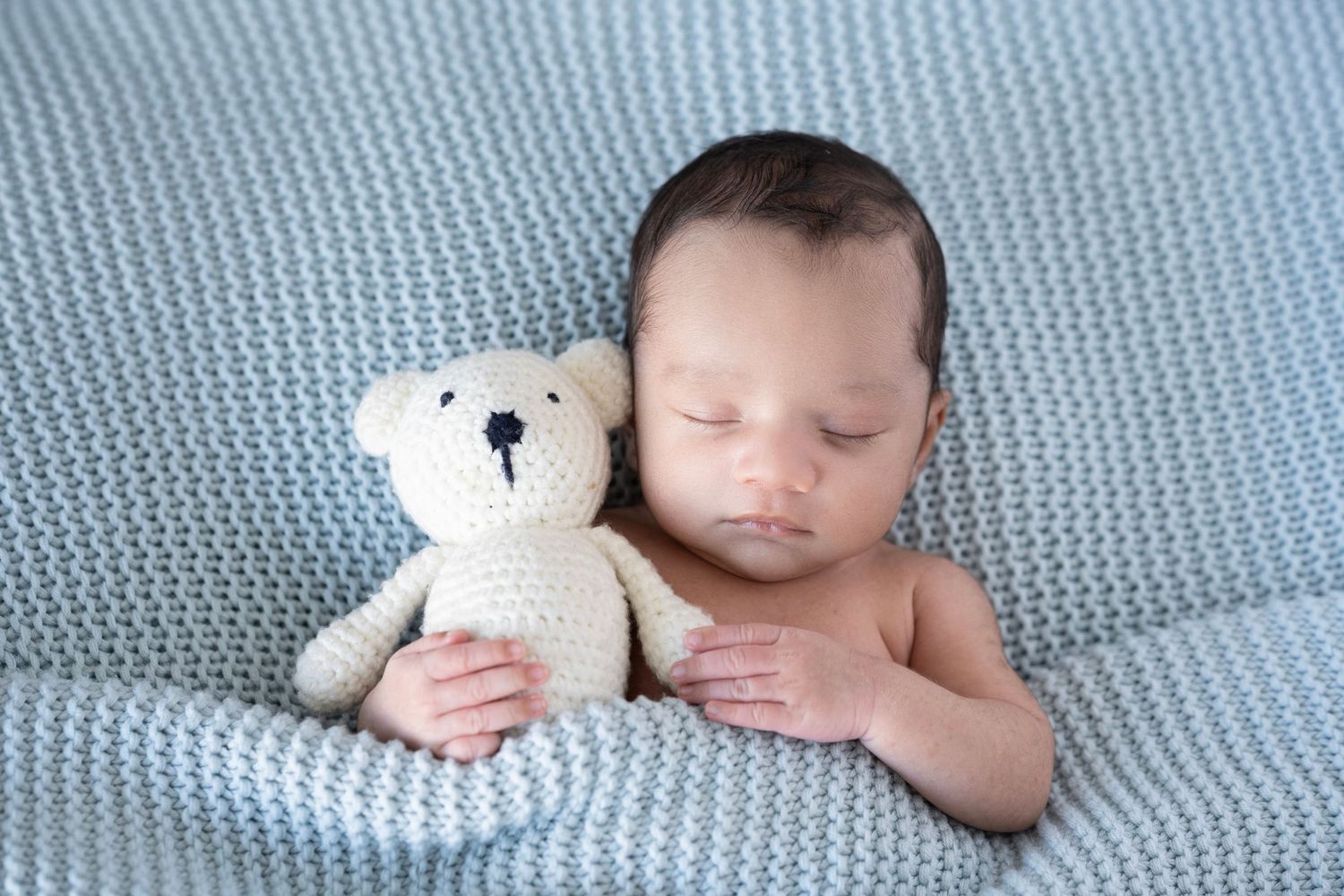 Sweet newborn photography on blue knitted blanket with white teddy bear.