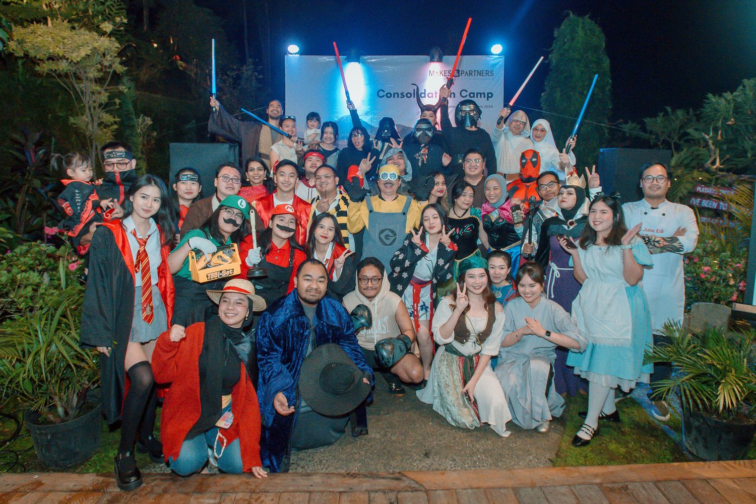 Large group in colorful costumes pose together at an outdoor Halloween or cosplay themed party at night.