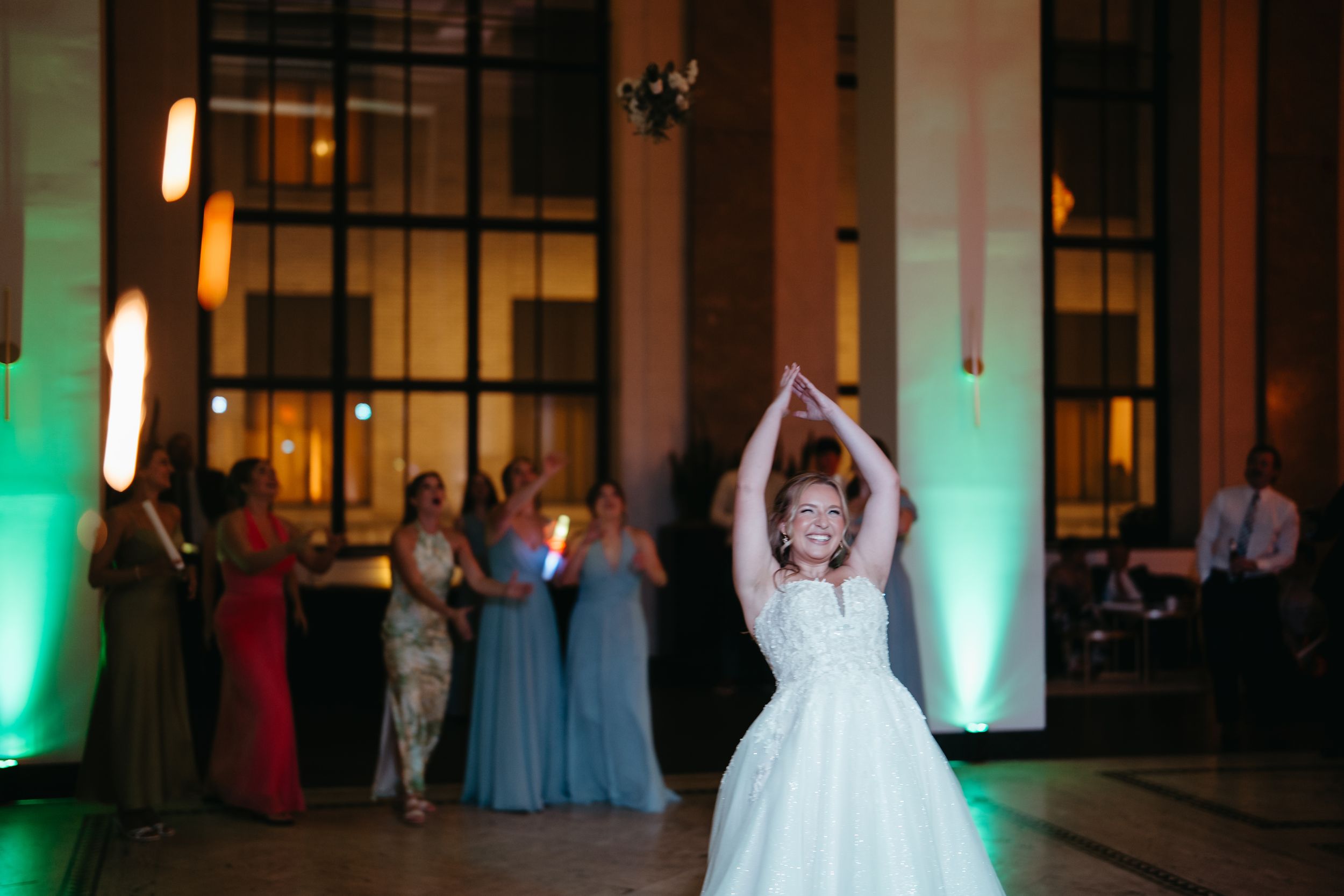 Young flower girl in white dress dances at elegant wedding reception with bridesmaids in blue gowns.
