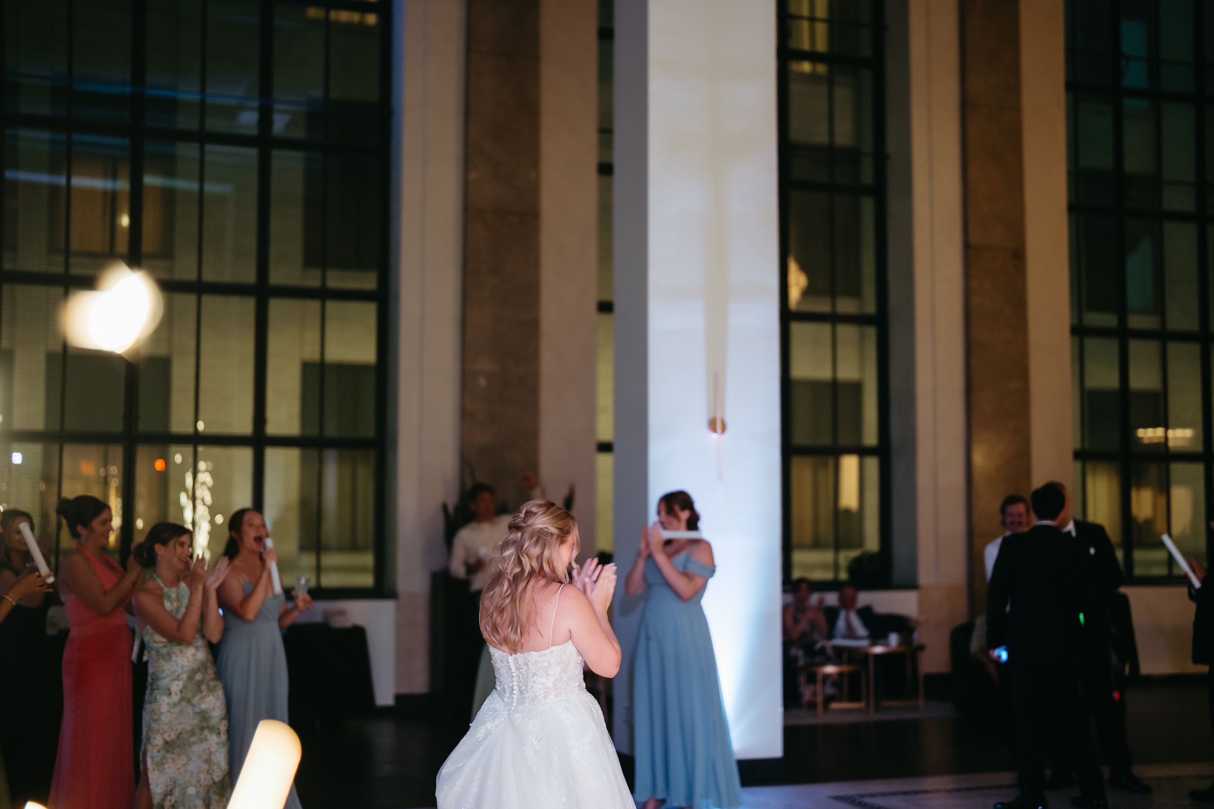 Bride and bridesmaid share a dance at elegant wedding reception in grand venue with large windows.