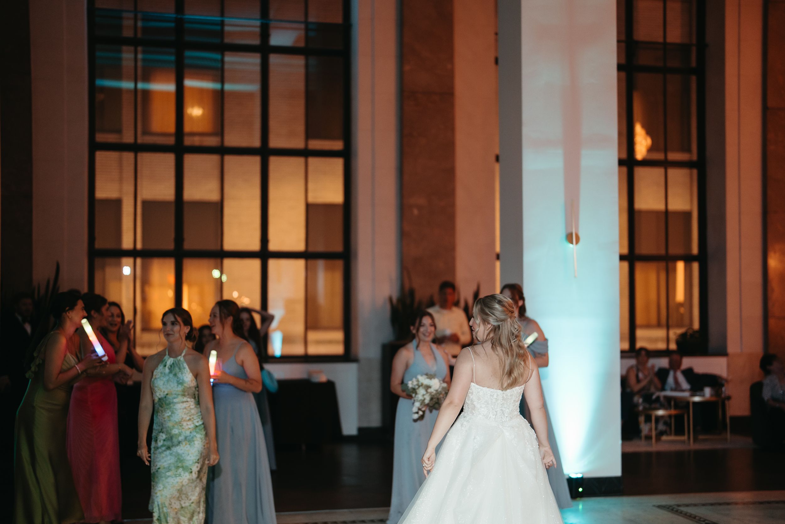 Bride in white gown dancing with bridesmaids in colorful dresses at elegant wedding reception venue.
