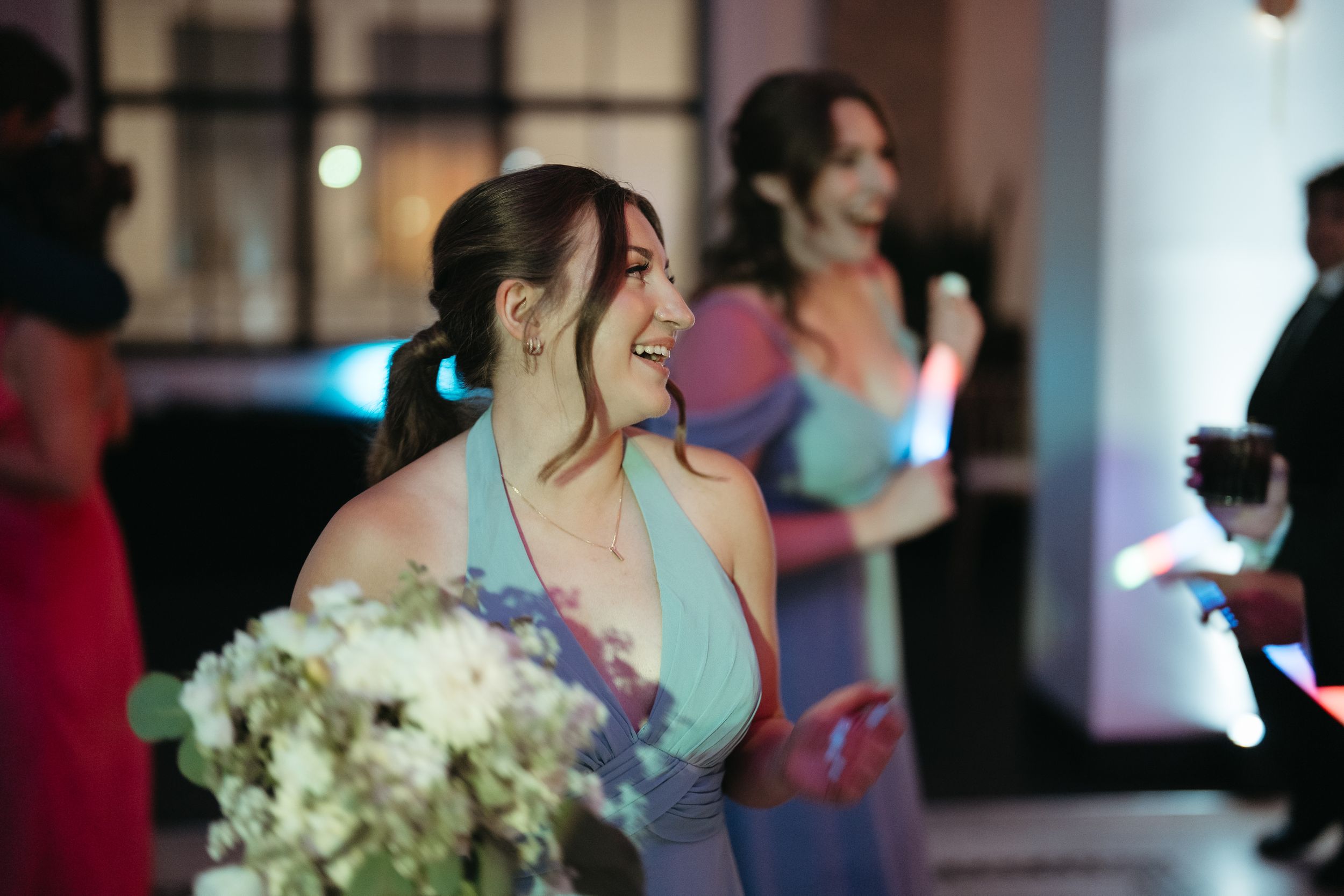 Bridesmaid in blue dress holding white bouquet, smiling and dancing at elegant wedding reception.