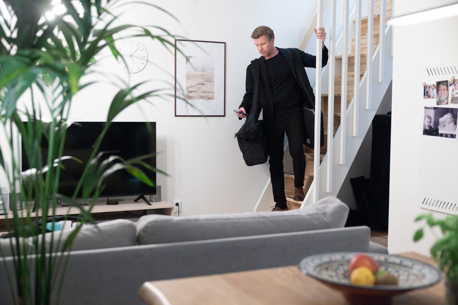 A man in black carrying a bag while walking through a modern minimalist living room.