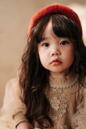 Young Asian girl with long wavy hair wearing a red headband and cream lace dress, gazing softly at the camera.