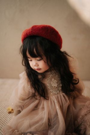 Young girl with dark hair wearing a red beret and sparkly tulle dress, looking down pensively.