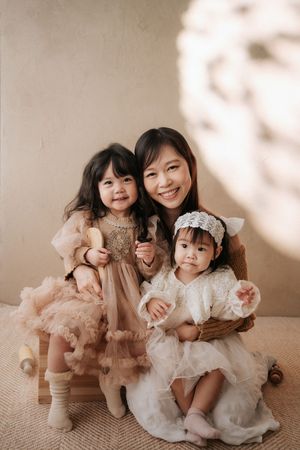 A smiling woman poses with two young girls in elegant dresses for a studio portrait photo.