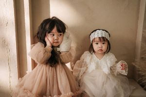 Two young girls in elegant dresses pose together, one in blush tulle and one in white lace with a headband.