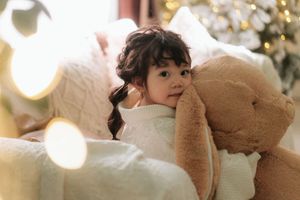 A young girl with pigtails hugs a large teddy bear on a couch near a Christmas tree.
