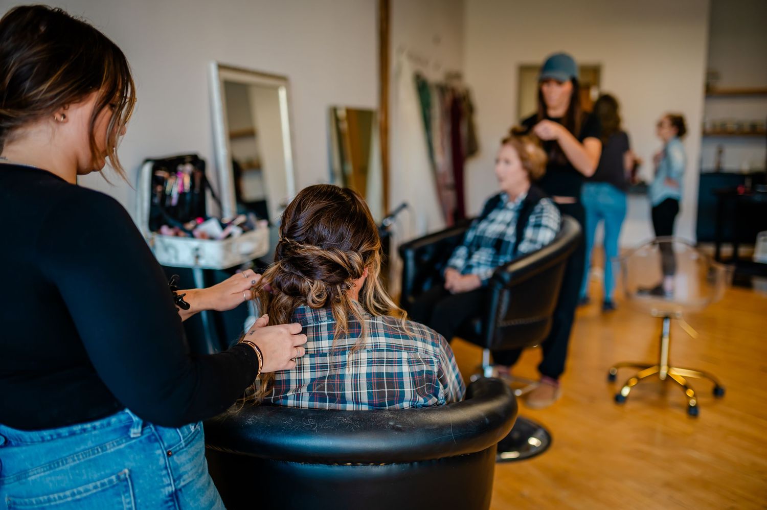 Hair stylist styling a client's hair in a modern salon with mirrors and another stylist working in the background.